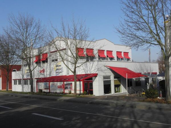 Modernes Firmengebäude mit roten Markisen und Jalousien für Sonnenschutz und Rollladen.