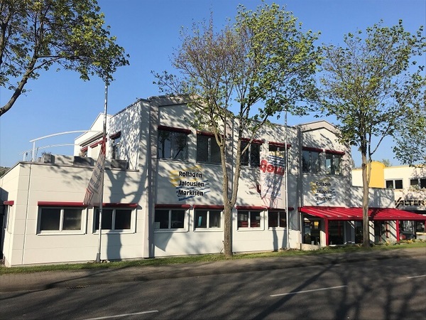 Modernes Firmengebäude mit Aufschrift für Rollladen, Jalousien und Markisen im Sonnenschein.