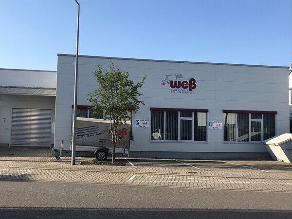 Firmengebäude mit Logo von WCB, Parkplatz, Anhänger und moderner Fassade bei Sonnenschein.