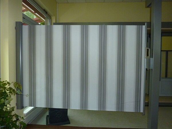 Seitenmarkise mit grauen und weißen Streifen als Sichtschutz auf Terrasse montiert.