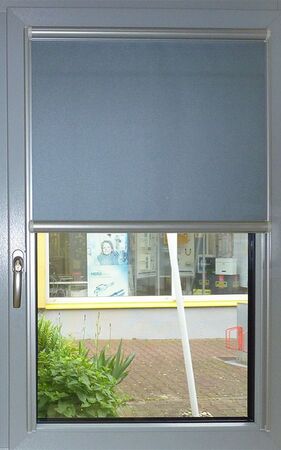 Fenster mit halb geschlossenem, grauem Rollo als Sicht- und Sonnenschutz im Innenbereich.