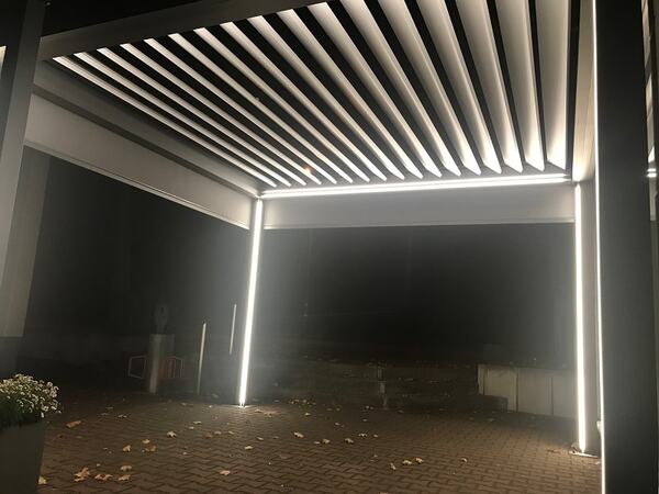 Moderne Terrassenüberdachung aus Aluminium mit LED-Beleuchtung bei Nacht beleuchtet.