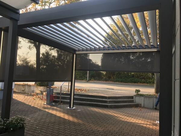 Moderne Terrassenüberdachung mit Lamellendach und seitlichen Sonnenschutz-Rollos im Freien.
