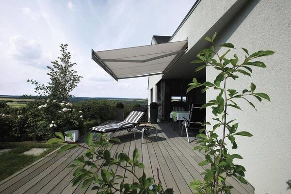 Moderne Terrasse mit Markise, Holzdielen, Gartenmöbeln und Blick ins Grüne im Sommer.