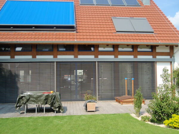 Modernes Einfamilienhaus mit Solaranlage, Außenjalousien und gepflegtem Garten.